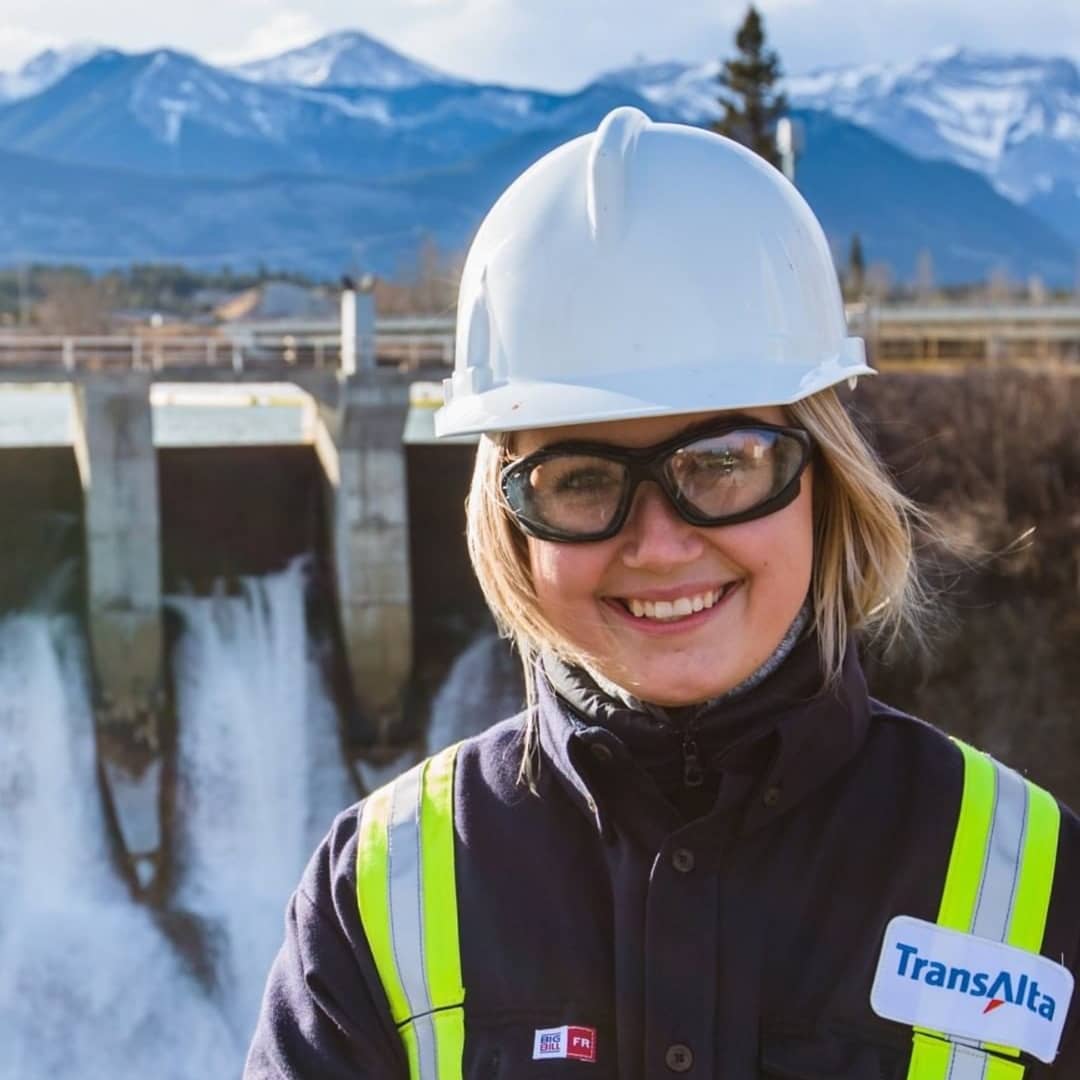 Young woman in hard hat stands in front of hydroelectric dam