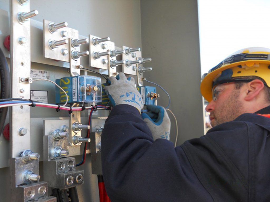 Male worker wearing gloves and hardhat works on electrical panel